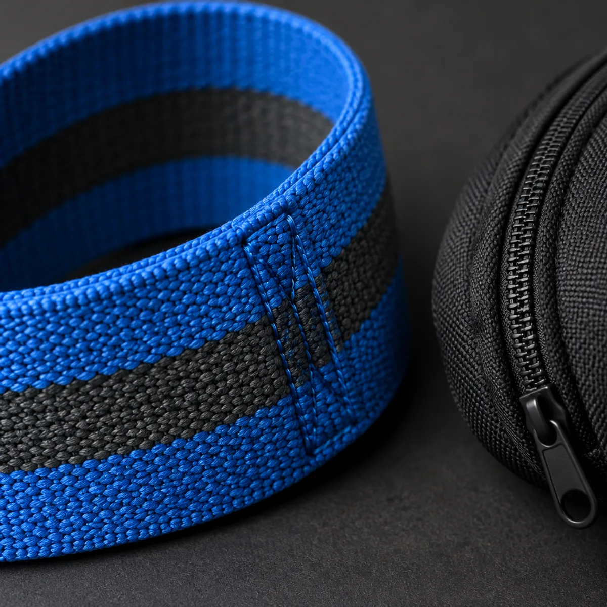 Close-up of woven blue and charcoal fabric resistance band with a stitched seam beside a pouch zipper
